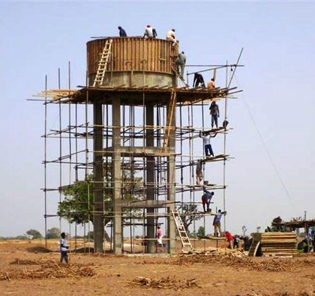 Equipe de maçons sur l'échafaudage en train de monter les seaux de béton