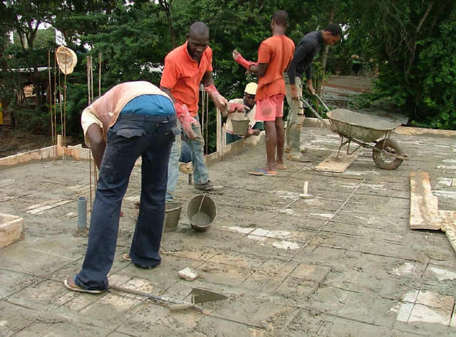 Equipe de maçons en train de couler la dalle en béton, servant de toiture pour le bloc sanitaire