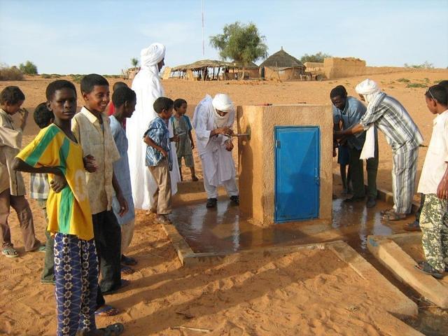 Des adultes viennent boire la première eau sortant de la borne-fontaine, sous le regard des enfants.