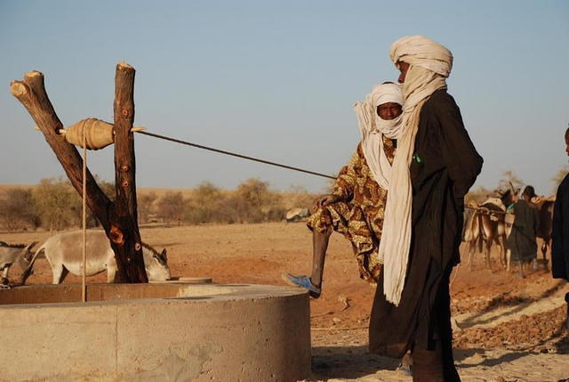 Deux hommes devant le puits, pendant qu'un âne tire la corde.