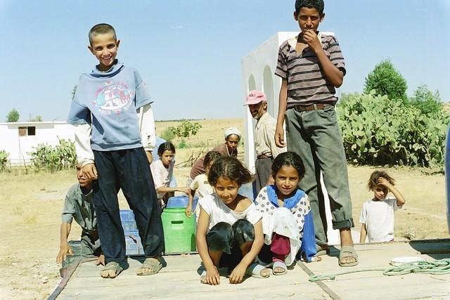 Enfants sur le plateau d'une charrette, et adultes à la borne-fontaine.