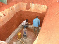 Après creusement dans le sol de latérite, les maçons réalisent les murs de la fosse.